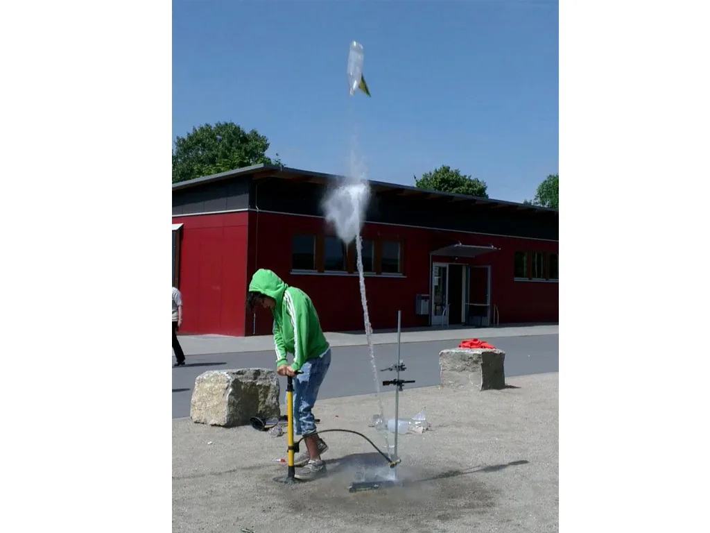Jugendlicher startet eine Wasserrakete auf dem Schulhof, der Wasserstrahl spritzt hoch.
